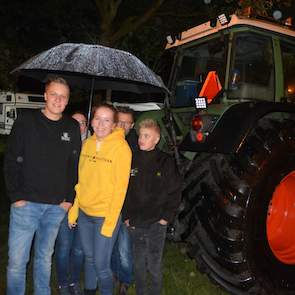 De familie Gunnik uit Alteveer (DR) staat met vijf man achter een trekker te schuilen onder een grote paraplu. Zoon Karlo (links) en zijn vriendin Laurien Kremer (gele trui) stappen straks in de trekker, zijn ouders en broertje zwaaien hen uit. „We moeten